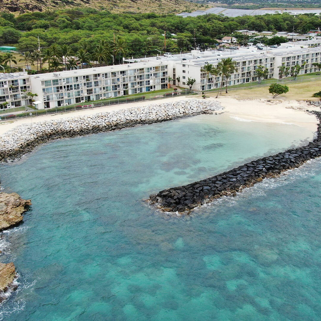 An ariel view of a rock revetment in blue water along an apartment building on the shore