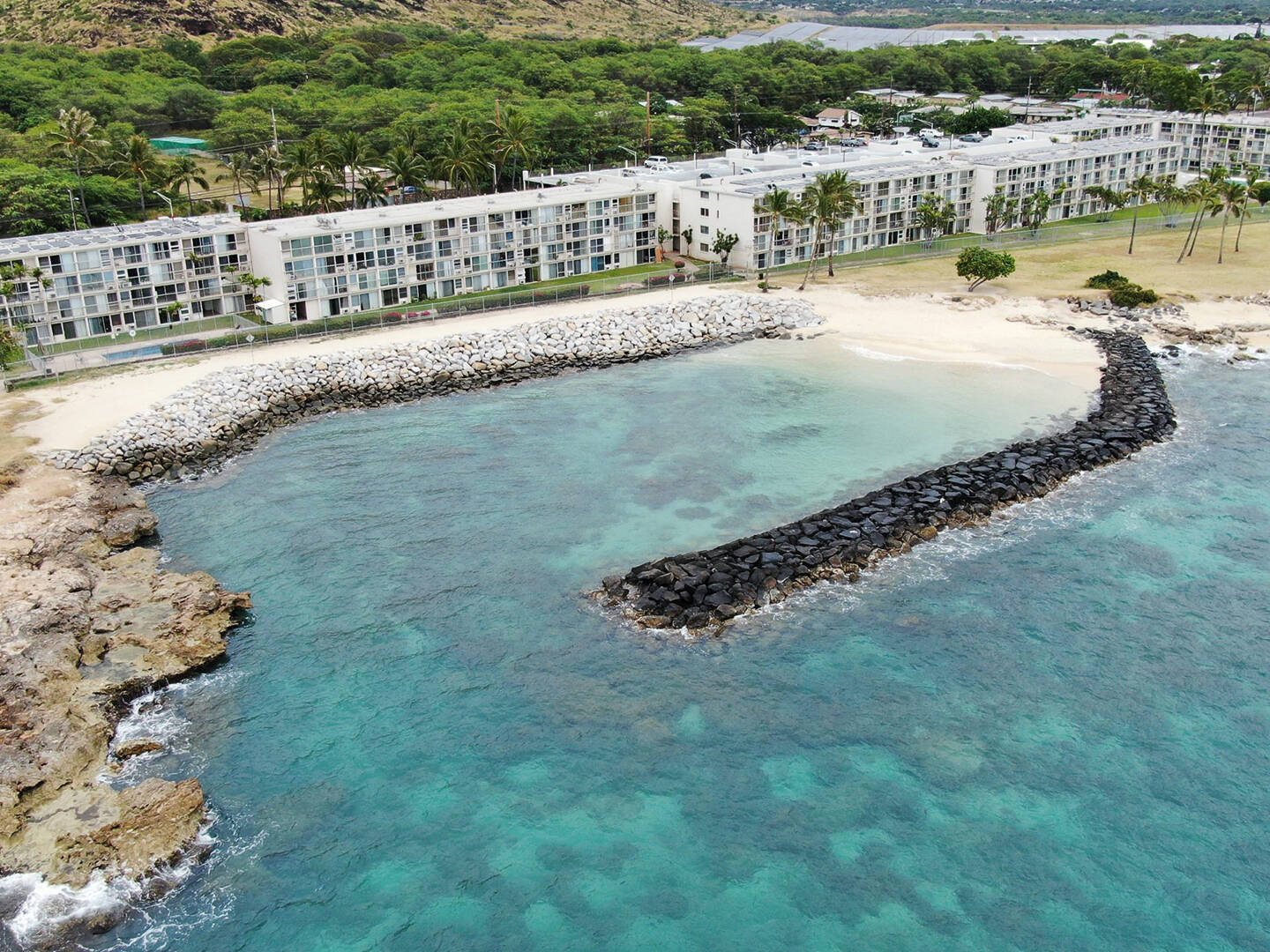 An ariel view of a rock revetment in blue water along an apartment building on the shore