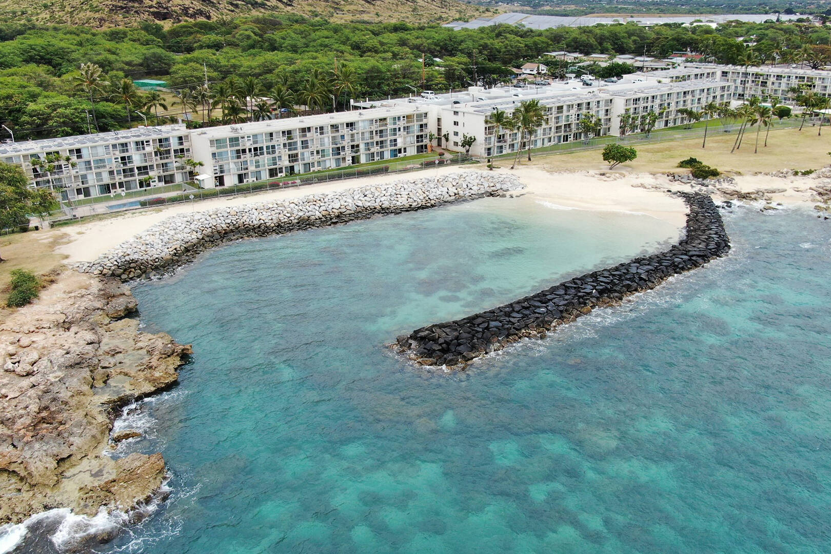An ariel view of a rock revetment in blue water along an apartment building on the shore