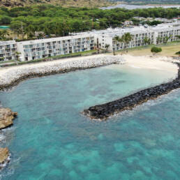 An ariel view of a rock revetment in blue water along an apartment building on the shore