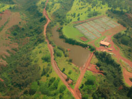 An aerial view of an Oahu landscape with red dirt roads and a large field surrounded by vegetation