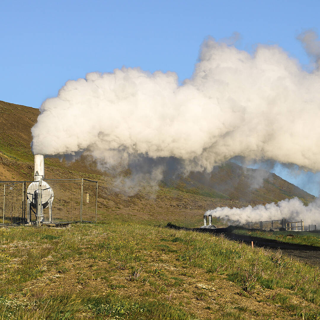 Two geothermal structures producing steam on a green landscape