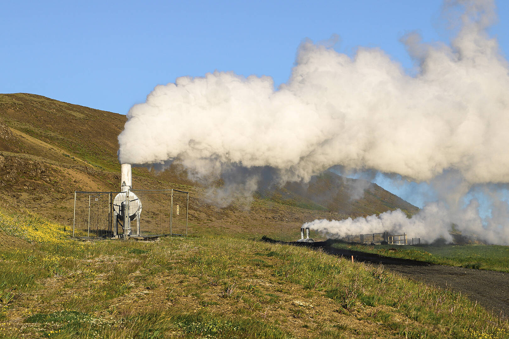 Two geothermal structures producing steam on a green landscape