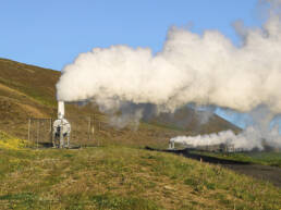 Two geothermal structures producing steam on a green landscape