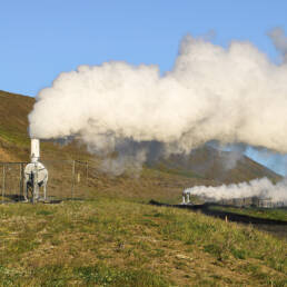 Two geothermal structures producing steam on a green landscape