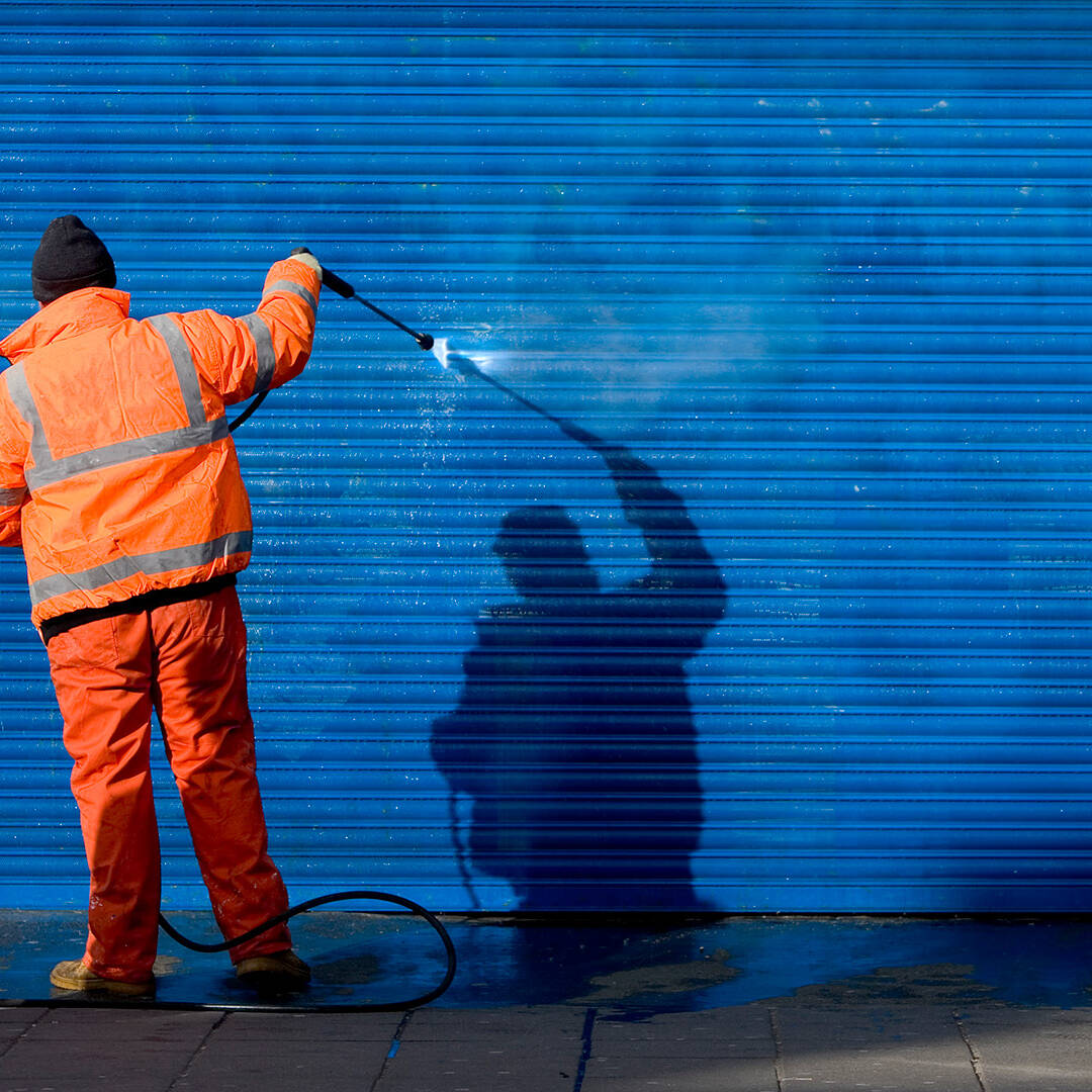 A man wearing a safety shirt and cleaning up graffiti