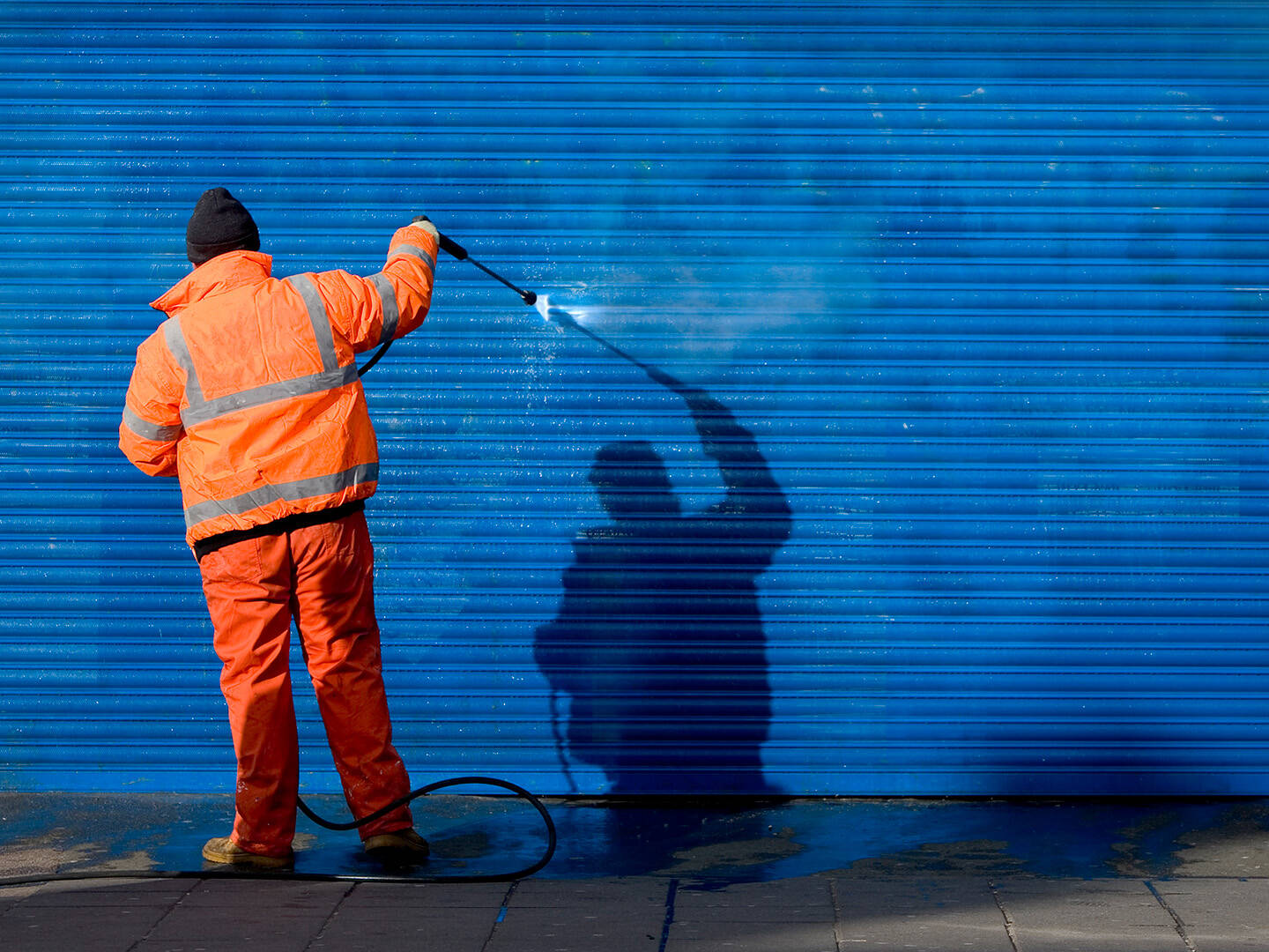 A man wearing a safety shirt and cleaning up graffiti