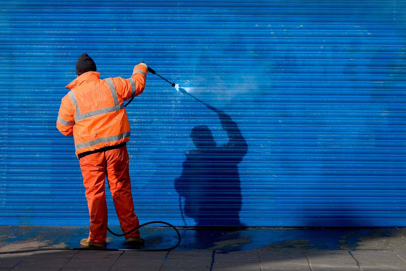 A man wearing a safety shirt and cleaning up graffiti
