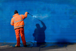 A man wearing a safety shirt and cleaning up graffiti