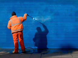 A man wearing a safety shirt and cleaning up graffiti