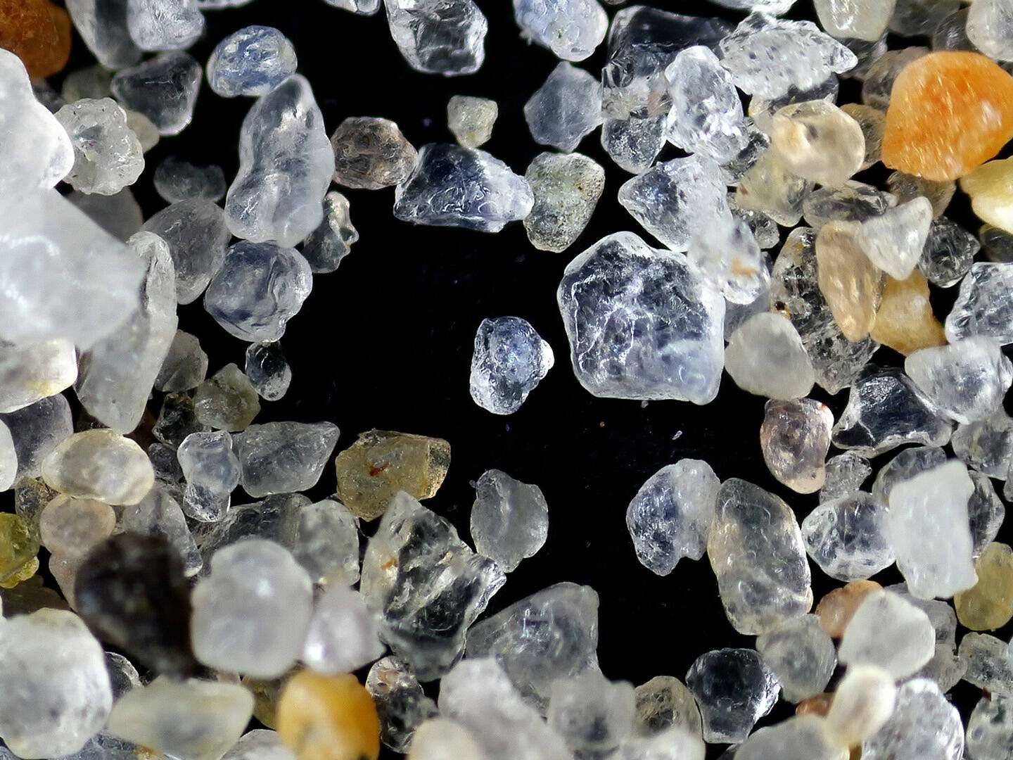 A microscopic view of grains of sand on a black background.