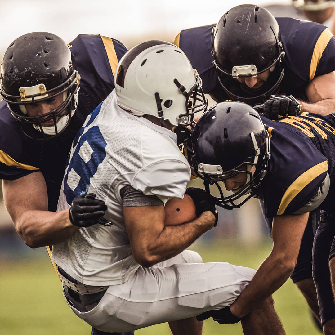 A football player in a white uniform being tackled by players in navy uniforms