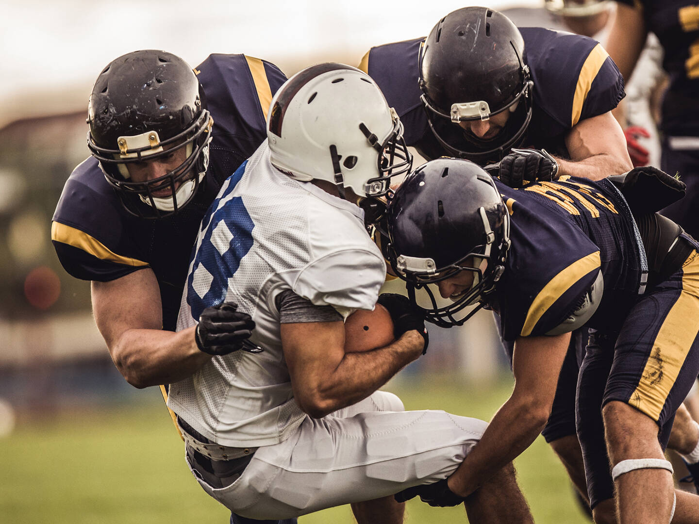 A football player in a white uniform being tackled by players in navy uniforms