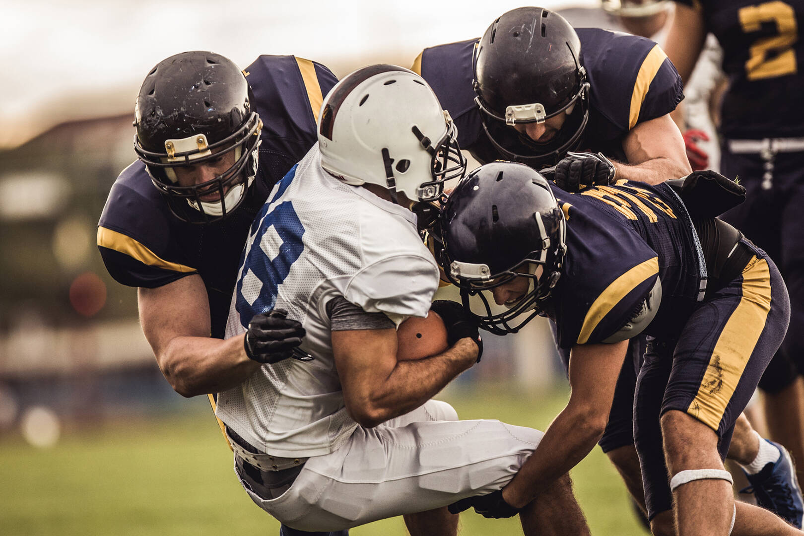 A football player in a white uniform being tackled by players in navy uniforms