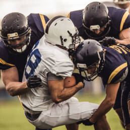A football player in a white uniform being tackled by players in navy uniforms