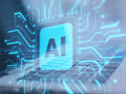 A 3D render of a blue computer chip with AI printed in the middle