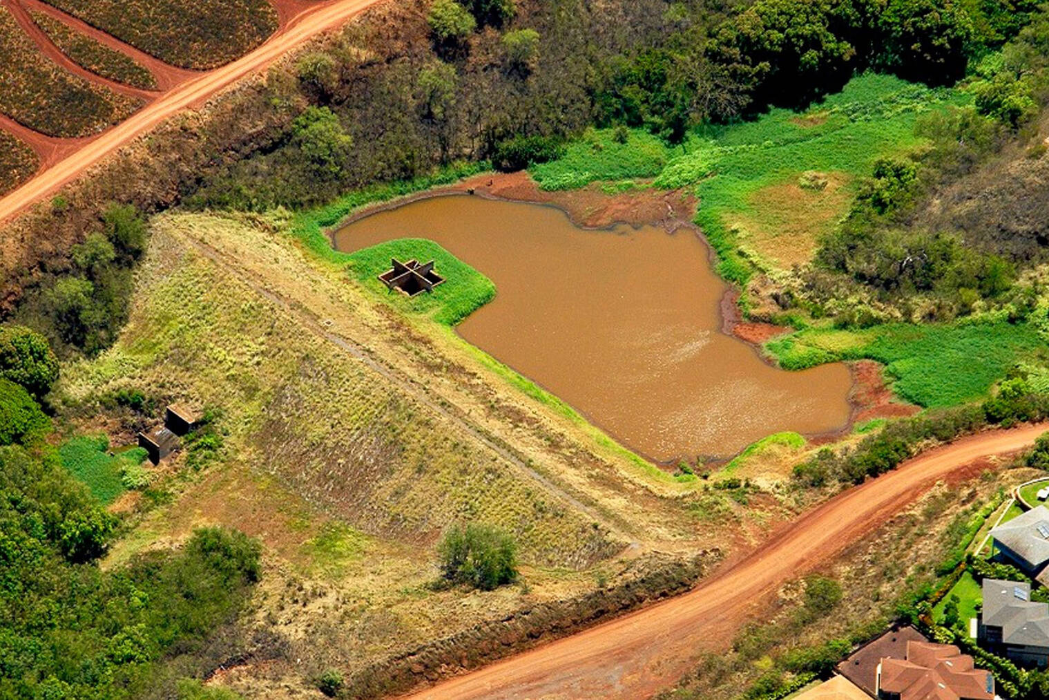 An ariel view of a water reservoir surrounded by red dirt and greenery