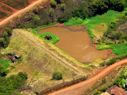 An ariel view of a water reservoir surrounded by red dirt and greenery