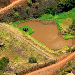 An ariel view of a water reservoir surrounded by red dirt and greenery