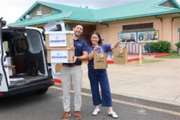 Two Oceanit employees holding boxes and bags of COVID-19 tests outside an Oahu school