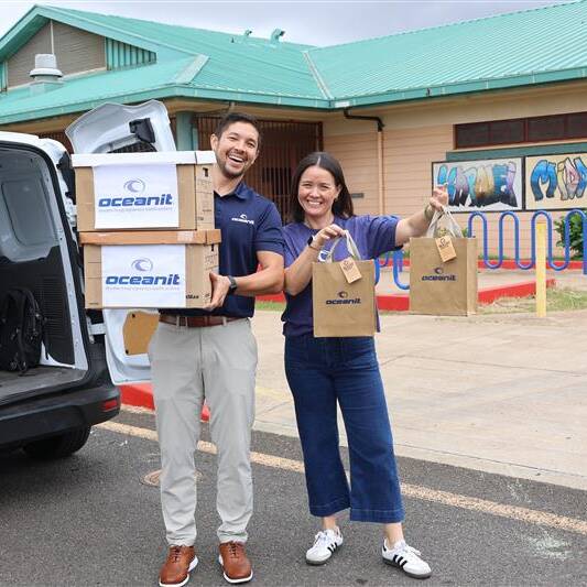 Two Oceanit employees holding boxes and bags of COVID-19 tests outside an Oahu school