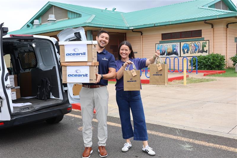 Two Oceanit employees holding boxes and bags of COVID-19 tests outside an Oahu school