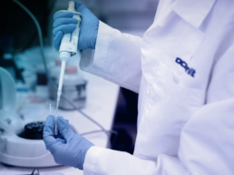 Someone in a white lab coat piping liquid into a test tube in a lab