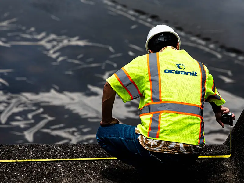 The back of a person wearing an Oceanit safety vest and hard had measuring a surface