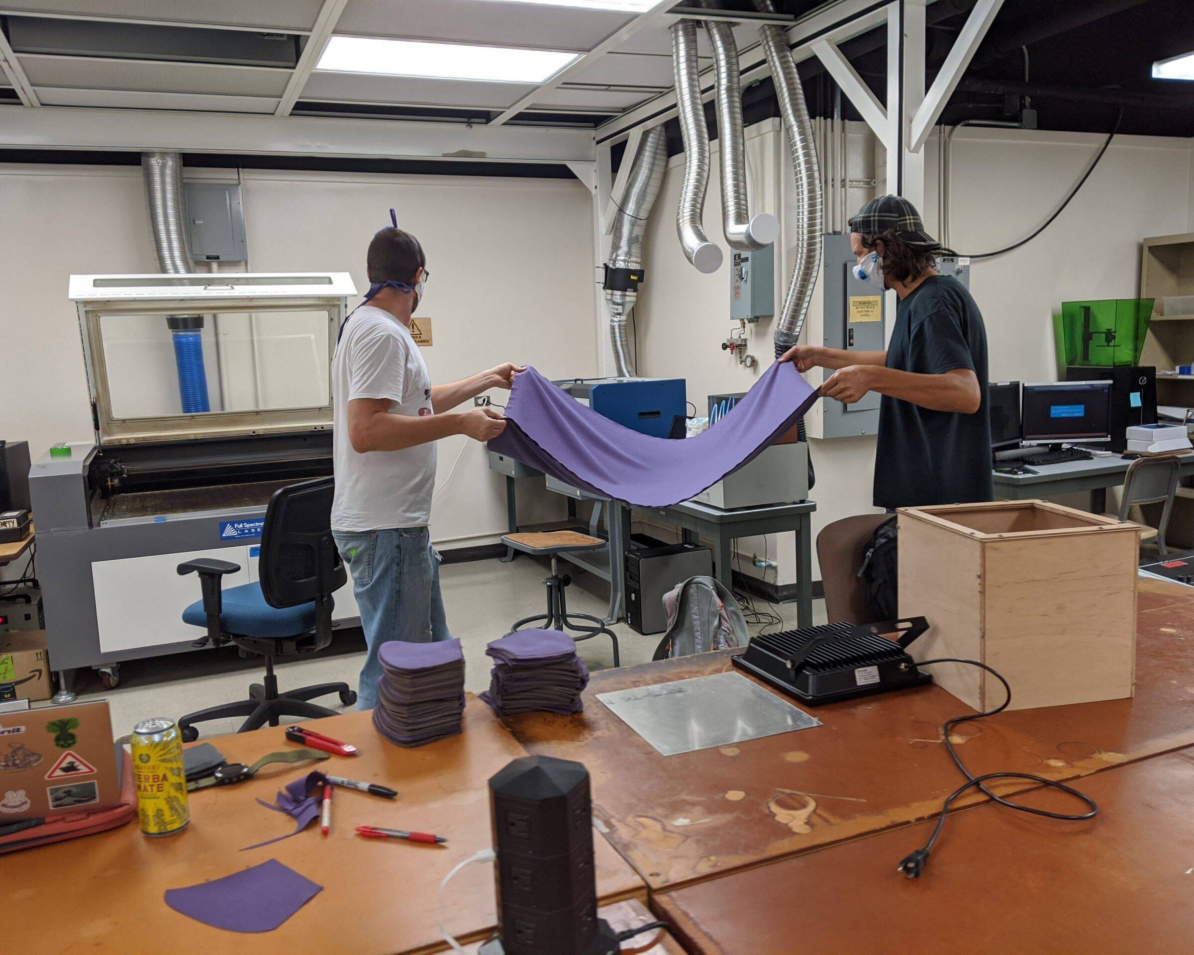 Two employees carrying a large piece of fabric to a machine for cutting