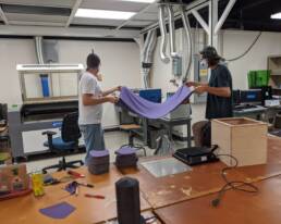 Two employees carrying a large piece of fabric to a machine for cutting