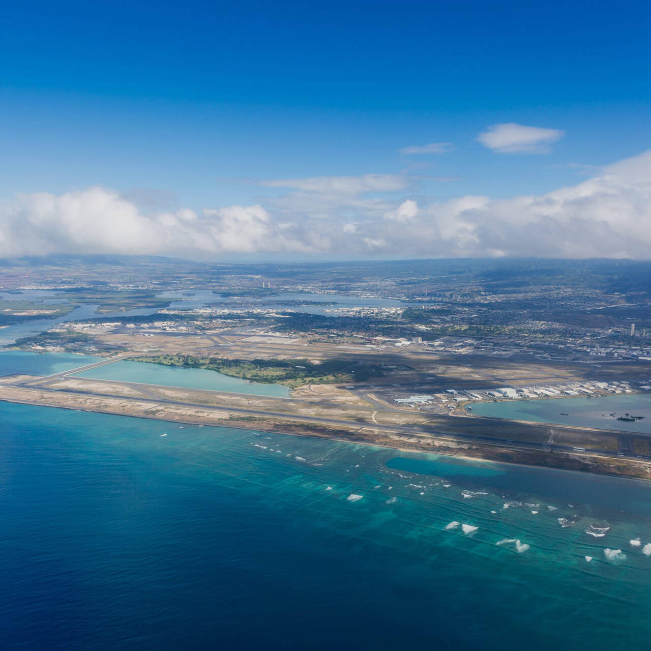 An aerial shot of the HNL airport runway as seen from the ocean