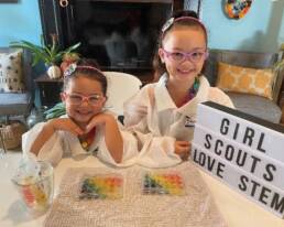 Two girl scouts displaying their science experiments with a sign that reads