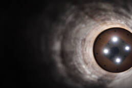 The inside of a pipeline, with lights illuminating the far end