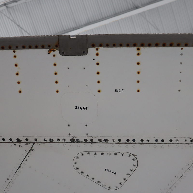 The underside of a plane wing with rusted screws