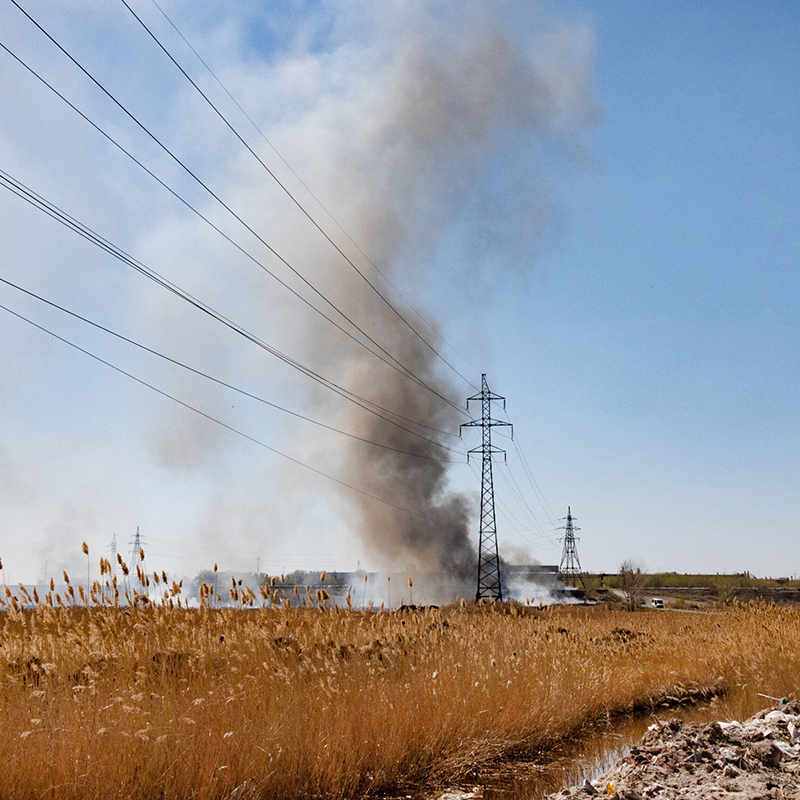 Smoke rising from the middle ground of a field containing power lines