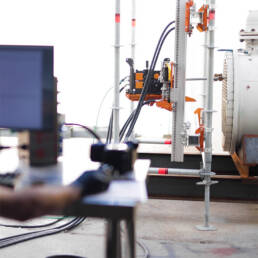 A camera apparatus on a rig near a heat exchanger, with a blurred person at a computer in the foreground