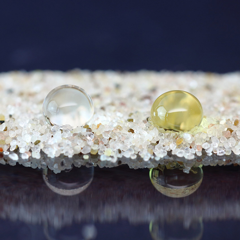 A close up of two beads of liquid beaded on a layer of sand