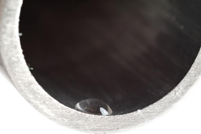 A pipe painted in a black material with a water droplet almost flat on the interior