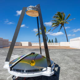 A MAMBA sensor on a concrete platform, with a low fence and palm trees in the background