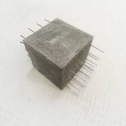 A concrete cube with rebar going through horizontally on a plain backdrop