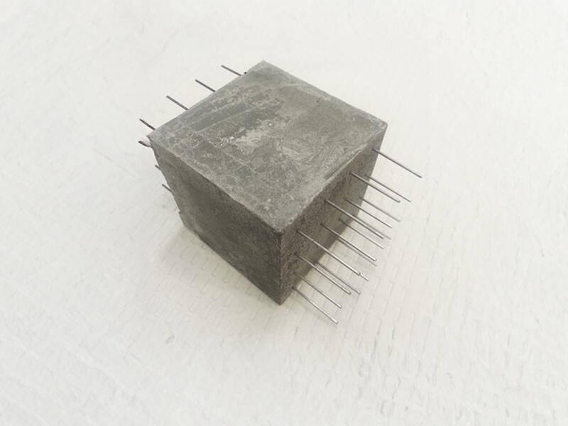 A concrete cube with rebar going through horizontally on a plain backdrop
