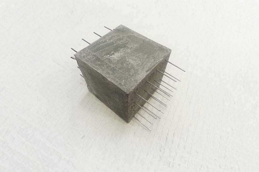 A concrete cube with rebar going through horizontally on a plain backdrop