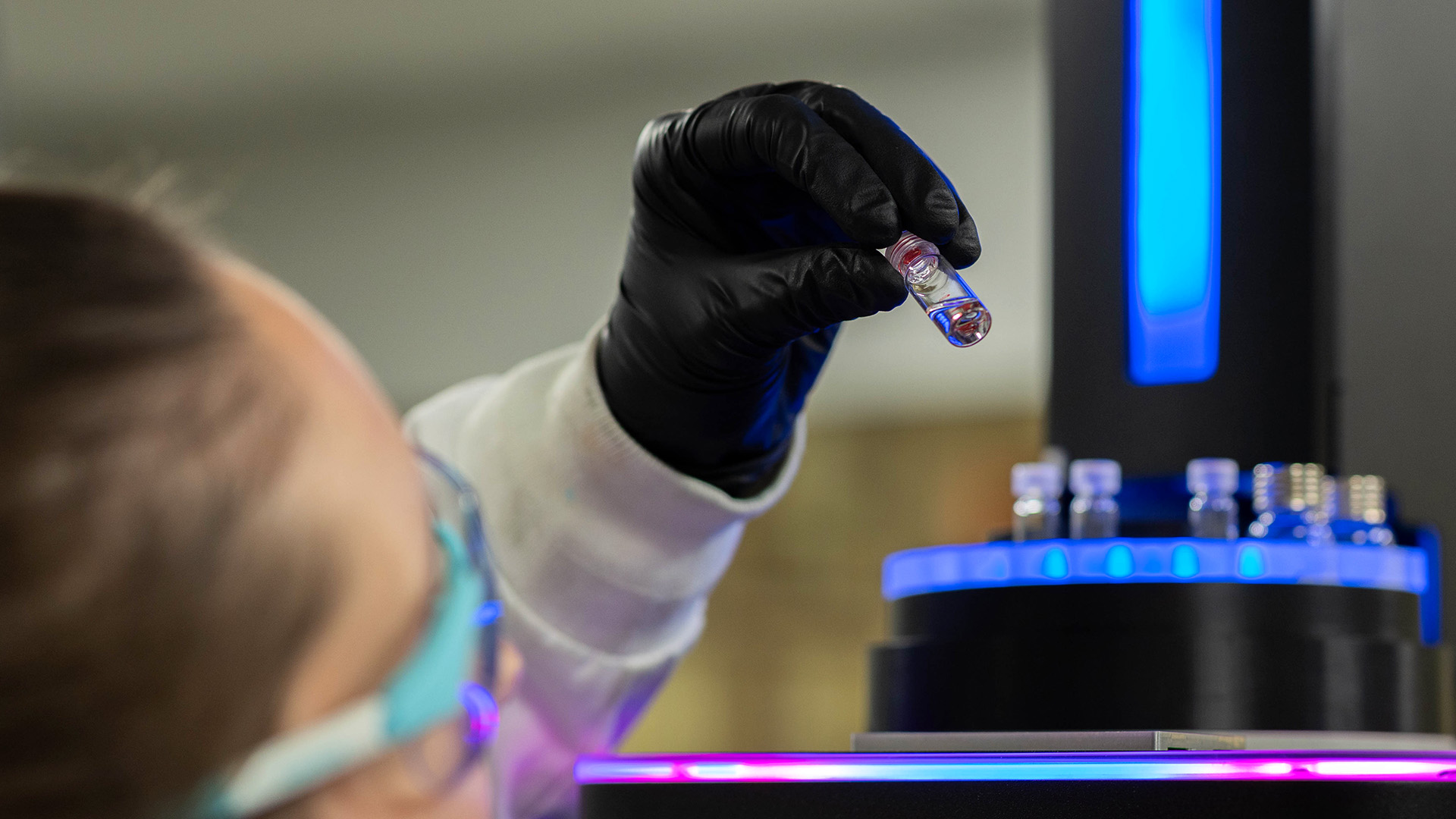 A lab worker holding up a vial of liquid against blue and purple lighting