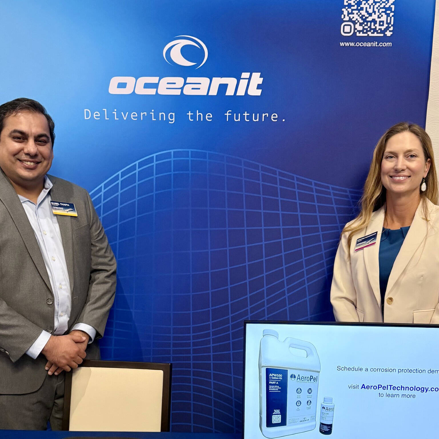 Two Oceanit employees standing in a booth with a blue Oceanit backdrop and an AeroPel jug