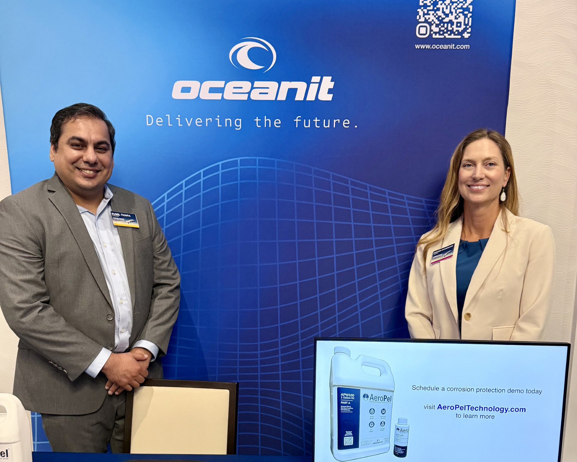 Two Oceanit employees standing in a booth with a blue Oceanit backdrop and an AeroPel jug