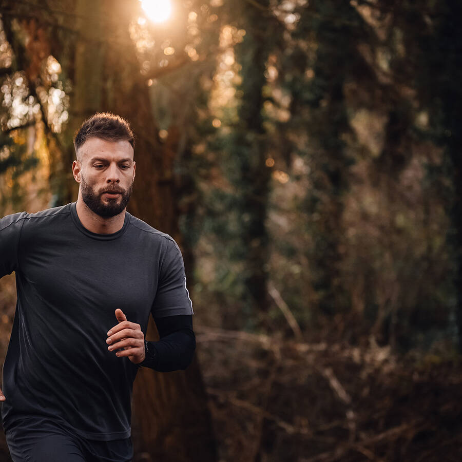 A man exercises by running through a forest at sunset